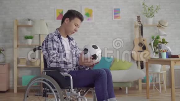悲伤的亚洲青年男子残疾人轮椅前运动员足球与足球视频的预览图