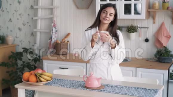 年轻漂亮的女人穿着白大褂在家厨房手里拿着杯子动作缓慢视频的预览图