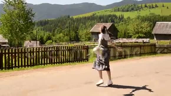 漂亮的年轻女人带着一个背包快乐地旋转夏日阳光明媚远处的村庄和青山视频的预览图