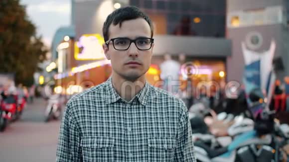 严肃的年轻商人戴着眼镜独自站在城市街道上的慢动作视频的预览图
