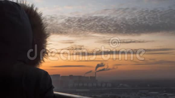 穿着一件带有毛茸茸的引擎盖的冬芥末皮夹克站在阳台上看日落的女性时光流逝视频的预览图