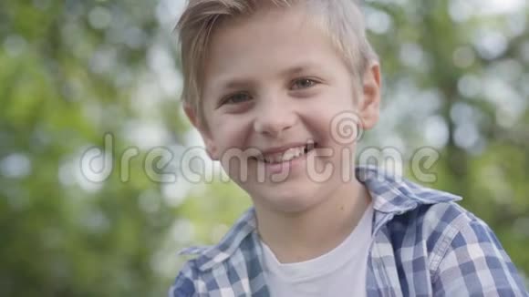 可爱的英俊男孩穿着格子衬衫坐在公园里看着镜头的特写肖像夏日休闲视频的预览图
