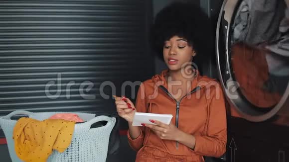 年轻有魅力的非洲裔美国妇女写做清单在记事本上坐在自助公共洗衣视频的预览图