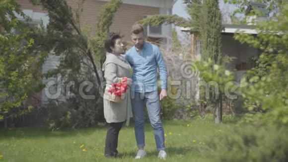 肖像成熟的女人拿着篮子手里拿着郁金香在后院和她的孙子说话成年孙子和成年孙子视频的预览图