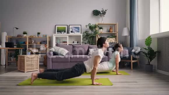 家庭中的男女青年在家练习瑜伽时练习狗的姿势视频的预览图