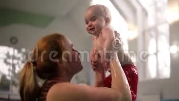 妈妈和她的宝宝穿着可爱的红色短裤在室内游泳池里玩得很开心在水里玩视频的预览图