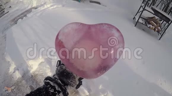 一个人手里拿着一颗冰做的粉红色的心冬天在外面在雪的背景下晴朗的晴天视频的预览图