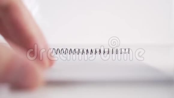 一个人慢慢地从一个垂直的笔记本上翻阅白色背景上挂着一个螺旋形的黑色页面视频的预览图