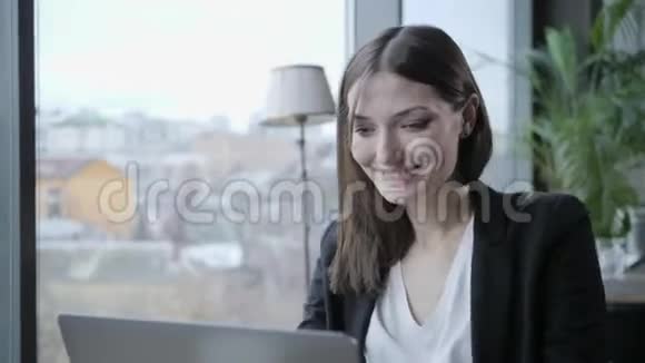 年轻的女人笑着坐在木桌旁的咖啡店里桌子上是灰色铝制笔记本电脑女孩博客视频的预览图