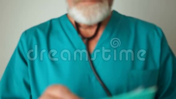 一个微笑的中年医生的肖像穿着绿色的医疗服帽子眼镜和听诊器在他的肩膀上灰色视频的预览图