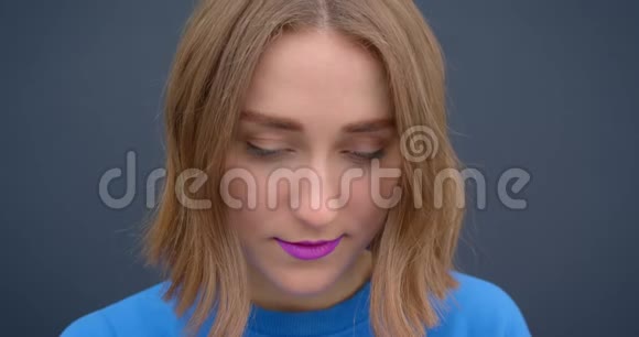 年轻的短头发女性的特写照片她涂着紫色口红微笑着看着灰色背景的镜头视频的预览图