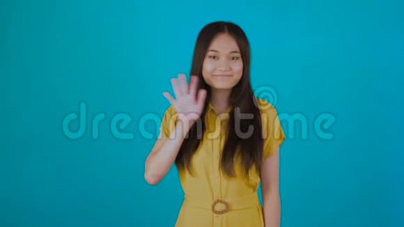 微笑可爱的亚洲女人打招呼挥手隔离在蓝色背景4K上视频的预览图