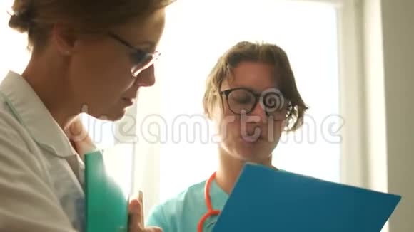两名女医生在一个医院的房间里交谈手里拿着笔记本脸上写着笔记医疗和保健视频的预览图