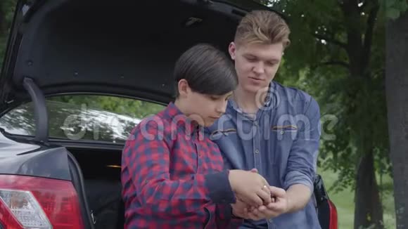 肖像年轻的父亲和他的儿子坐在户外的汽车后面那个检查螺丝司机的男孩那个人视频的预览图