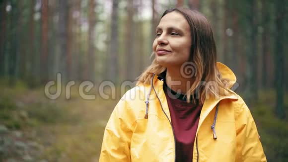 一位穿着亮黄色夹克的年轻女子站在雨林中的肖像视频的预览图