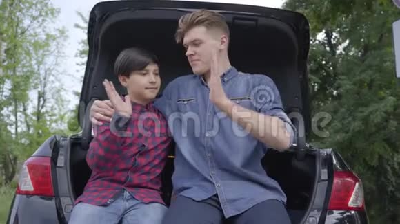 两个兄弟坐在户外的汽车后面那个男人拥抱男孩人们互相看着而不是走进视频的预览图