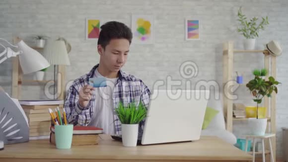 穿着衬衫的亚洲年轻人用笔记本电脑上的银行卡输入数据视频的预览图
