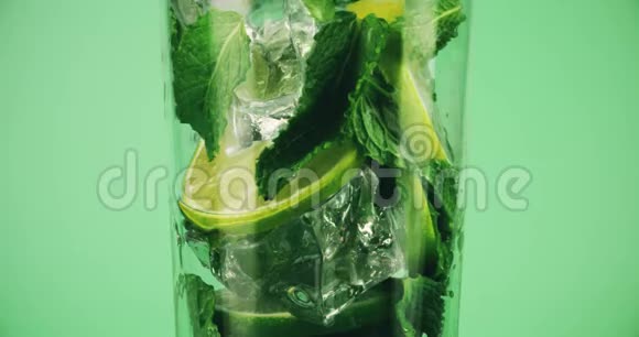 在绿色背景下用杯子做莫吉托鸡尾酒用红色拍摄宏观慢动作视频的预览图