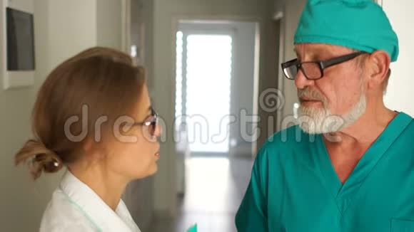 两个医生在走廊里说话头发灰白留着胡子戴着眼镜的年轻女子门诊工作人员视频的预览图