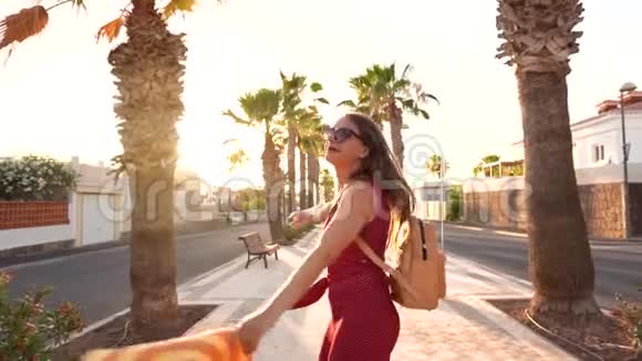 快乐的女人在日落时快乐地沿着棕榈巷奔跑挥舞着一顶黄色的大帽子慢动作视频的预览图