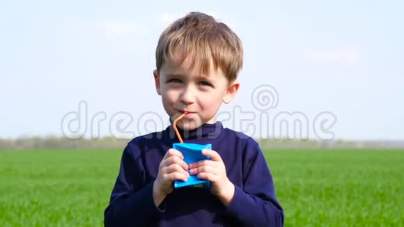 一个快乐的孩子从一个未知制造商的纸板箱里喝果汁这个男孩在户外喝酒的概念视频的预览图
