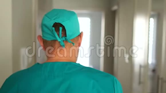 一位穿着医疗服的严肃疲惫的医生走在医院走廊上坐在椅子上脱下帽子视频的预览图