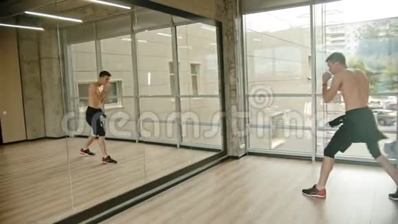 一个运动的赤膊男子站在画室里在镜子前训练他的拳击视频的预览图