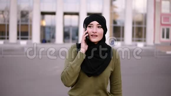 一位身穿传统头巾和绿色连衣裙的穆斯林年轻女性在智能手机上与朋友交谈视频的预览图