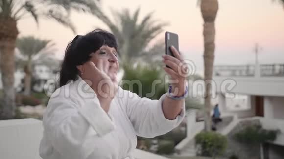 快乐的白种人高级妇女在热带度假胜地休息并打视频电话使用智能手机慢动作视频的预览图