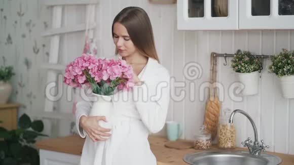 快乐的年轻女子穿着白色浴袍捧着一束鲜花嗅着它微笑着视频的预览图