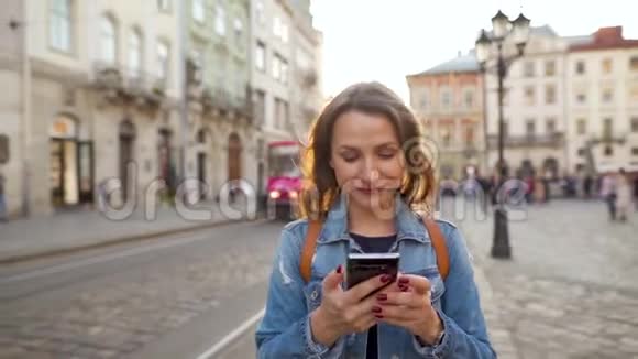 日落时分女人用智能手机走在老街上有轨电车在后台交流社会视频的预览图