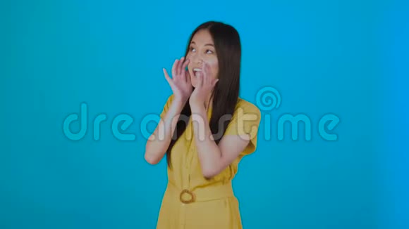 漂亮的亚洲年轻女子用双手捂住嘴讲述一个秘密在浅蓝色背景下被隔离视频的预览图