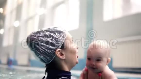 年轻的母亲带着孩子在室内游泳池游泳快乐的妈妈带着爱带着红色的孩子玩视频的预览图