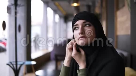 年轻穆斯林妇女戴着头巾坐在咖啡馆里的肖像看着一边思考决心纠正她的头视频的预览图