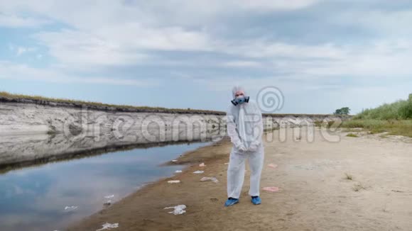 一个穿着防护服和呼吸器的人站在塑料垃圾桶中靠近一条干涸的河流挥动他的手视频的预览图