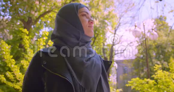 年轻漂亮的穆斯林女性戴着头巾看着镜头在公园的室外开心地微笑视频的预览图
