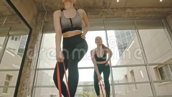 两个健康的女人站在工作室里用一条拉伸皮带训练她们的手把皮带拉起来视频的预览图
