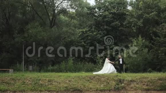 一对穿着婚纱的夫妇穿过树林一对夫妇在树之间散步新娘的婚纱婚礼视频的预览图