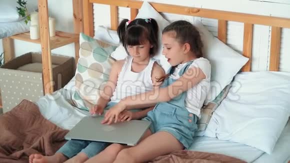 两个小女孩坐在床上打开笔记本电脑看动画片慢动作视频的预览图