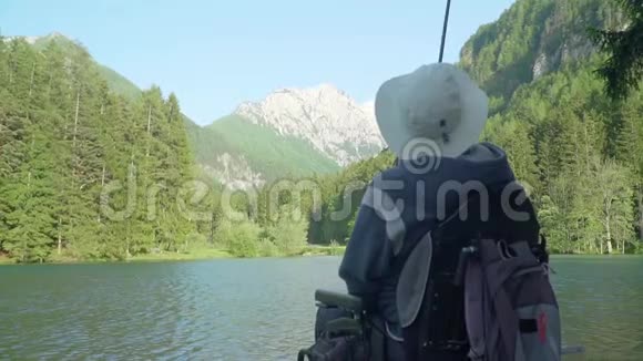 在森林和森林附近美丽的湖泊里残疾渔夫坐着电动轮椅在后面缓慢的动作视频的预览图