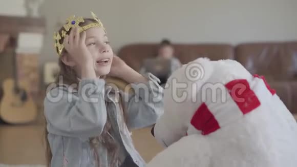 可爱的女孩在玩北方熊玩具给他戴上皇冠她的孪生兄弟在沙发上玩手提电脑视频的预览图