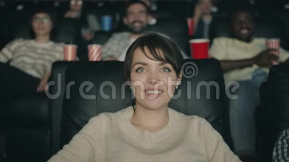 在电影院笑着看电影的漂亮黑发美女的肖像视频的预览图