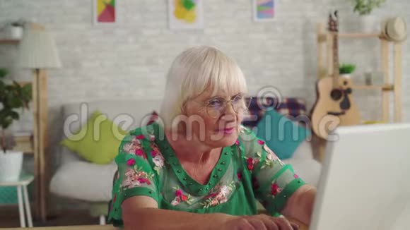 体贴的老妇人坐在客厅里用笔记本电脑视频的预览图
