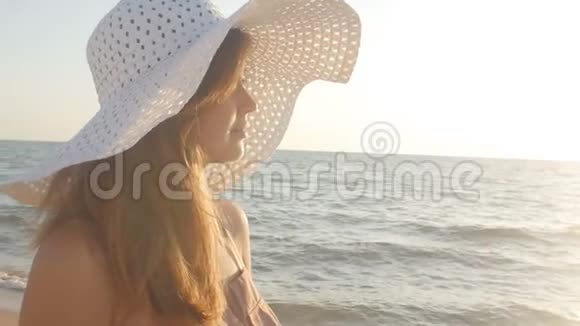 一个年轻女子戴着一顶宽边帽戴着一顶大海背景下的太阳帽在日出时享受大自然视频的预览图