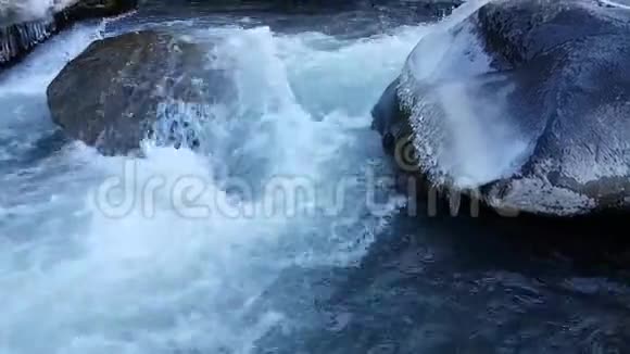 霜冻期间的暴风雨河在水中的大巨石上的冰柱水的快速电流秋天冬天春天视频的预览图
