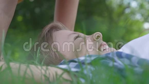 特写肖像可爱的小女孩亲吻躺在草地上的男孩的额头一对幸福的孩子有趣搞笑视频的预览图