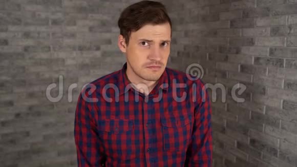 一个穿格子衬衫的年轻帅哥在灰砖背景上感到悲伤视频的预览图