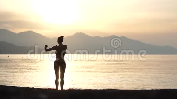 早晨日出时一个穿泳衣的女孩在海滨做运动视频的预览图