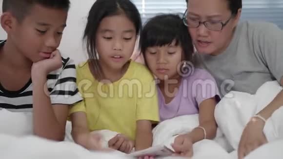 年轻的母亲和她的女儿和儿子正在卧室里玩手机视频的预览图
