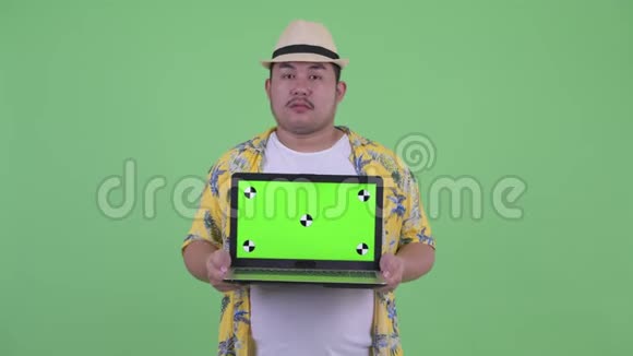 快乐的年轻超重的亚洲游客一边思考一边展示笔记本电脑视频的预览图
